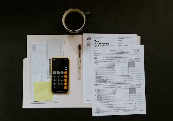 bunch of paperwork, a coffee mug, a pen and a phone that has its calculator opened up