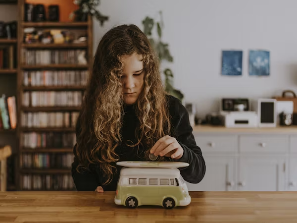 A little girl is putting her coins in a piggy bank that looks like a bus